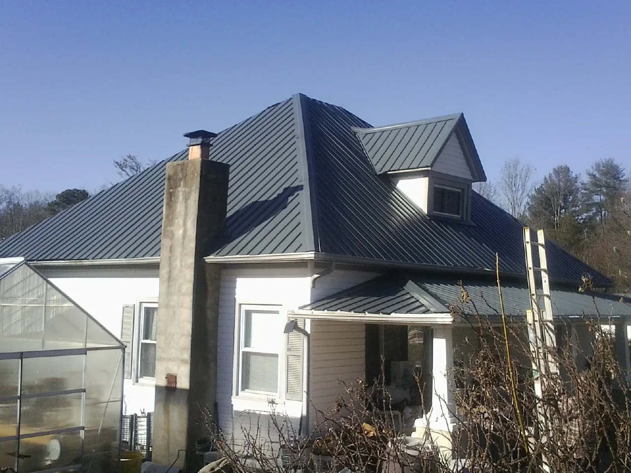 Dark blue standing seam metal roof on a white farmhouse with dormer — Slate & Tile Roof Repair by Roofing Brothers in Royalton