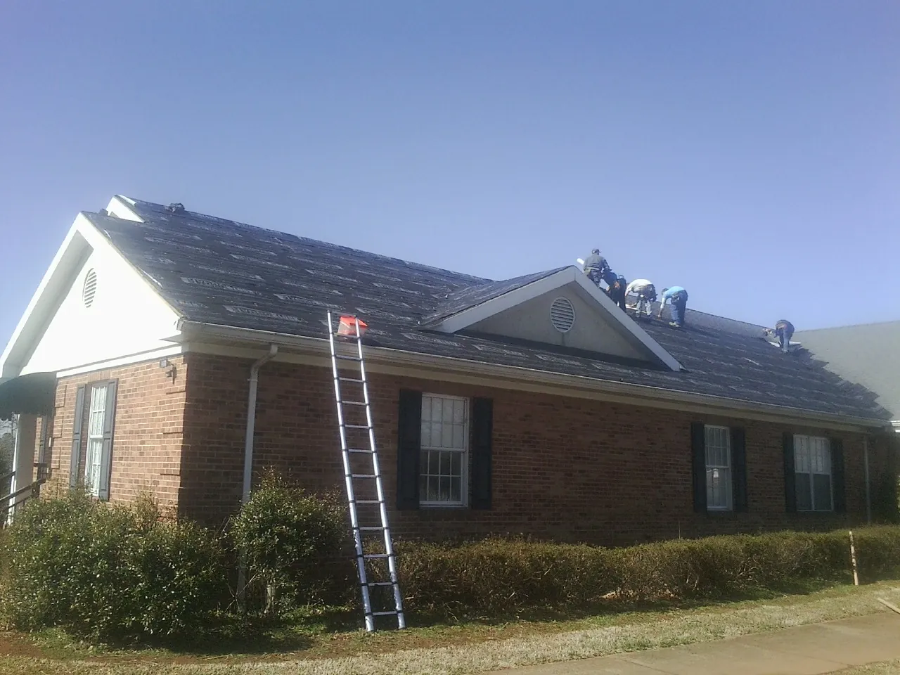 Crew tearing shingles off a brick ranch roof with a ladder set — Metal Roof Repair work by our crew in Royalton