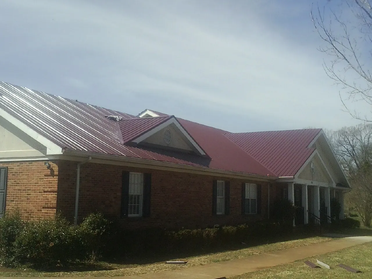 Red metal roof with gabled entries on a long brick building, from a Hail Damage Roof Repair job in Royalton