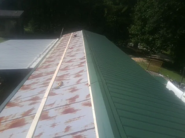Old rusted panels beside newly installed green metal roofing — Wind Damage Roof Repair by Roofing Brothers in Royalton