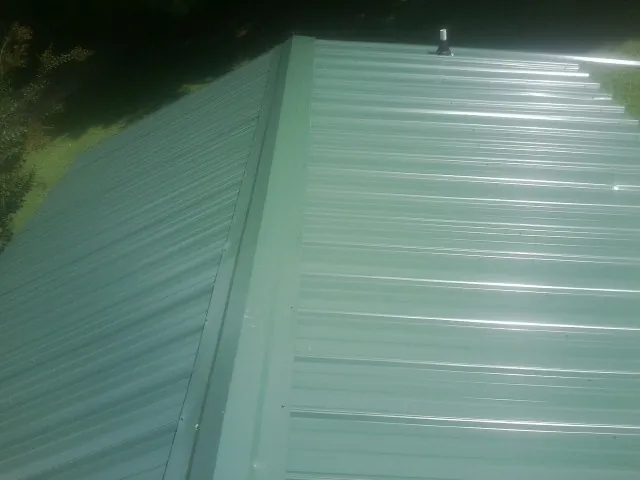 New green metal panels meeting at the ridge of a roof — Flat Roof Repair work by our crew in Royalton