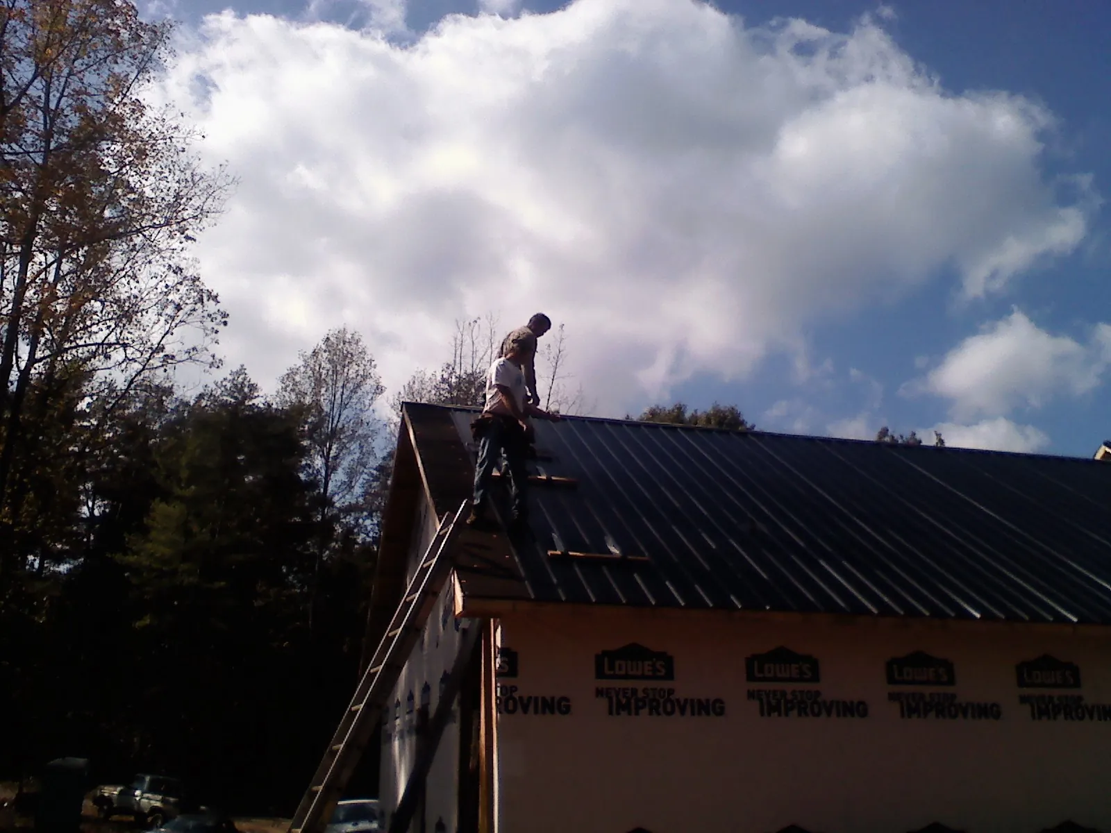 Roofer fastening dark metal panels high against a cloudy sky, from a Roof Inspection job in Royalton