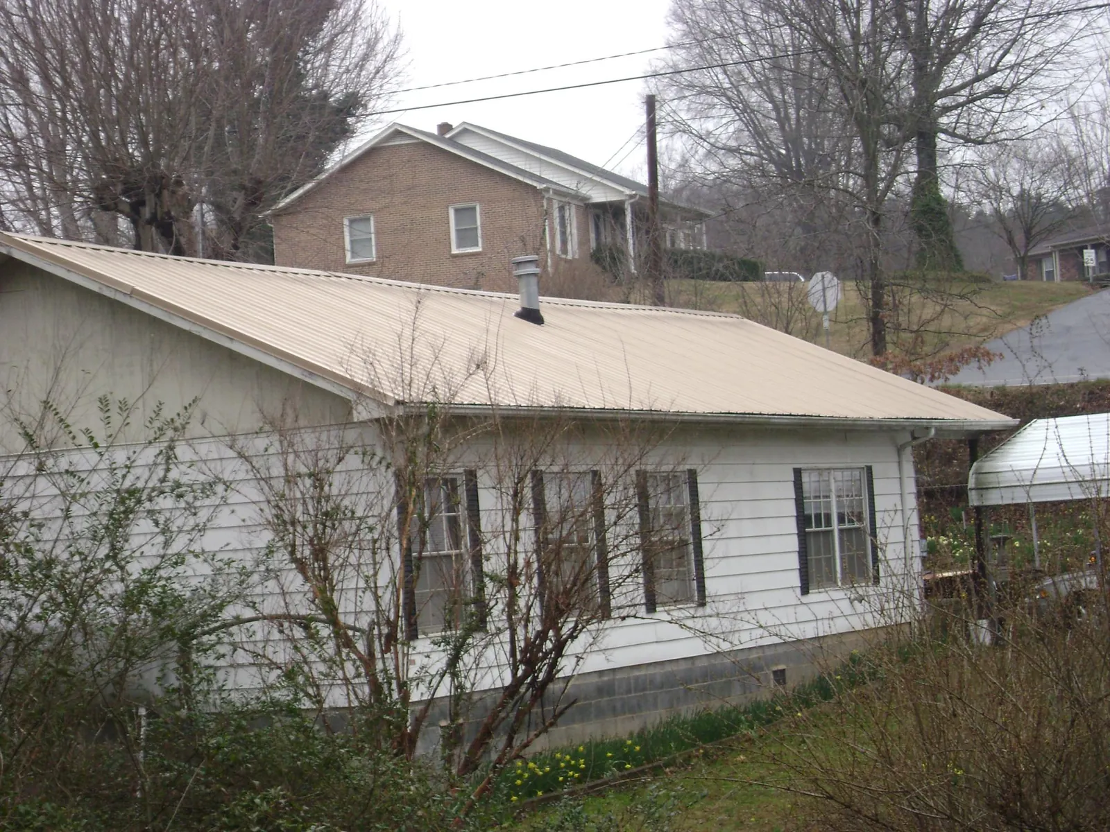 Tan metal roof on a white sided house set into a hillside — Commercial Roofing by Roofing Brothers in Royalton